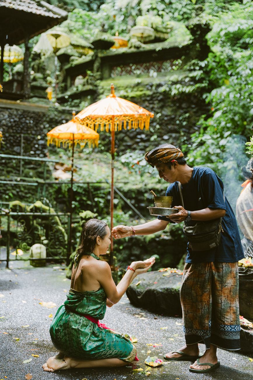 A woman receiving a blessing under a painted umbrella, petals in her hands