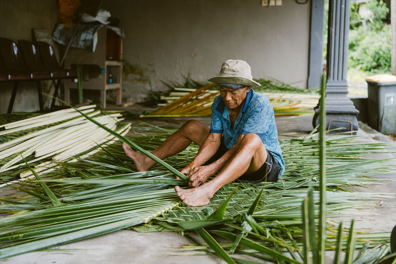A craftsman splitting palm leaf on the ground for offerings
