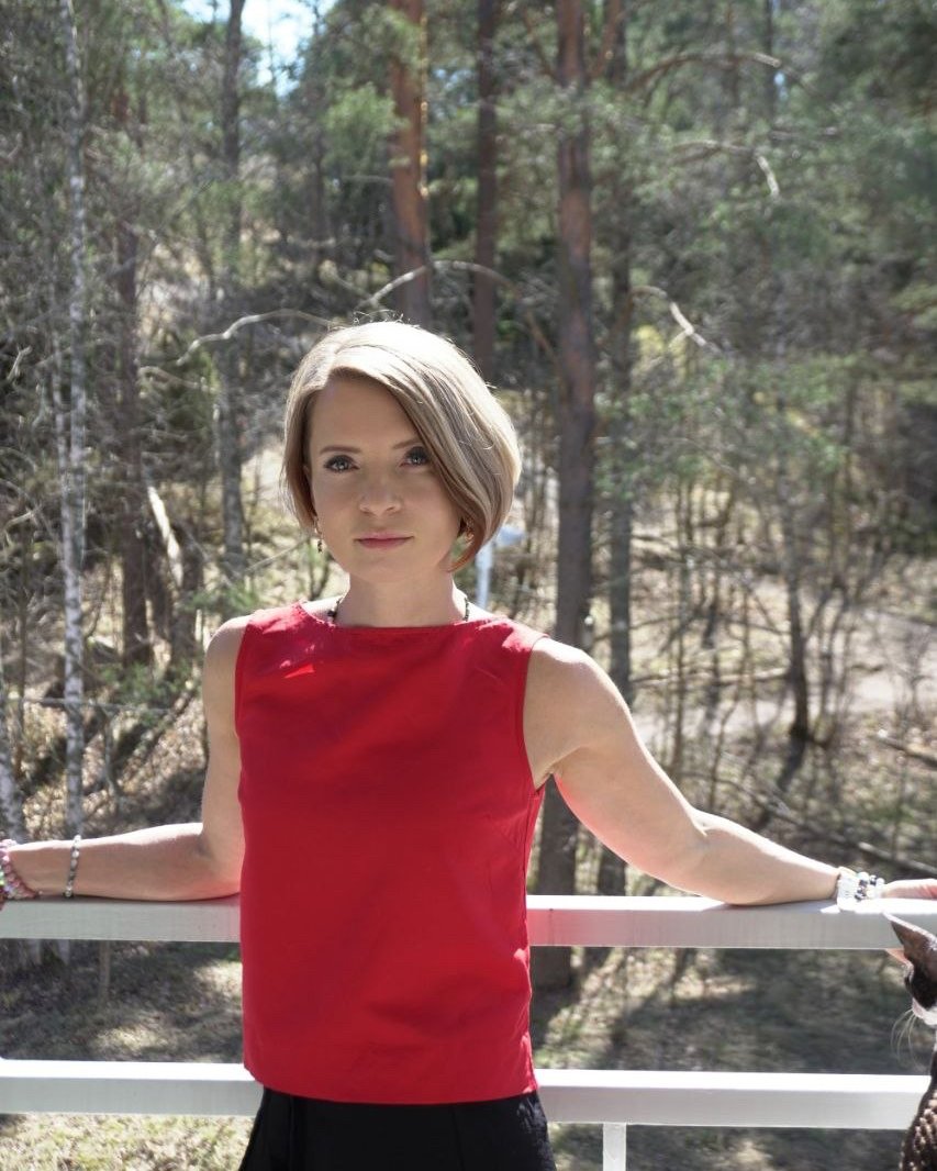 Natasha standing at a railing with pine forest behind