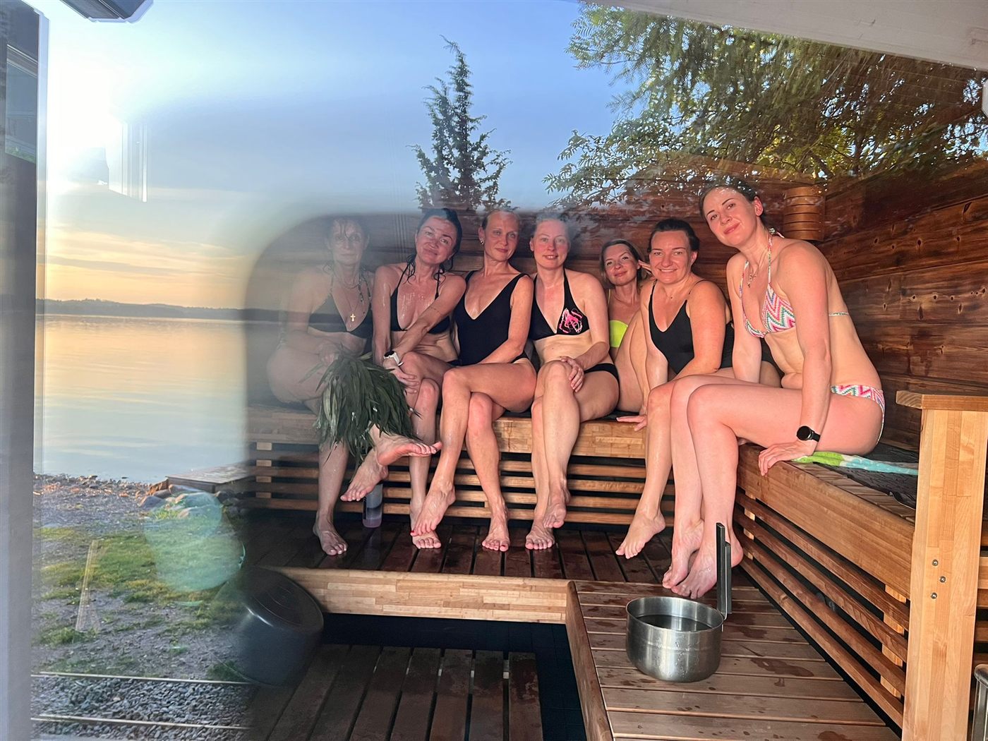 A group sitting together on a sauna bench, a lake sunset layered over the frame