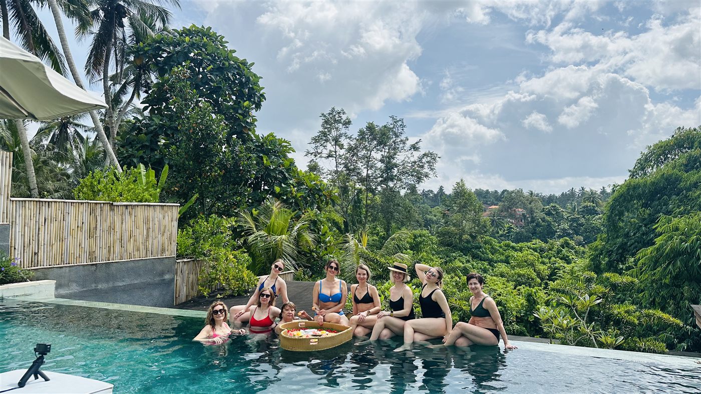 A group gathered at the edge of an infinity pool looking out over dense green valley