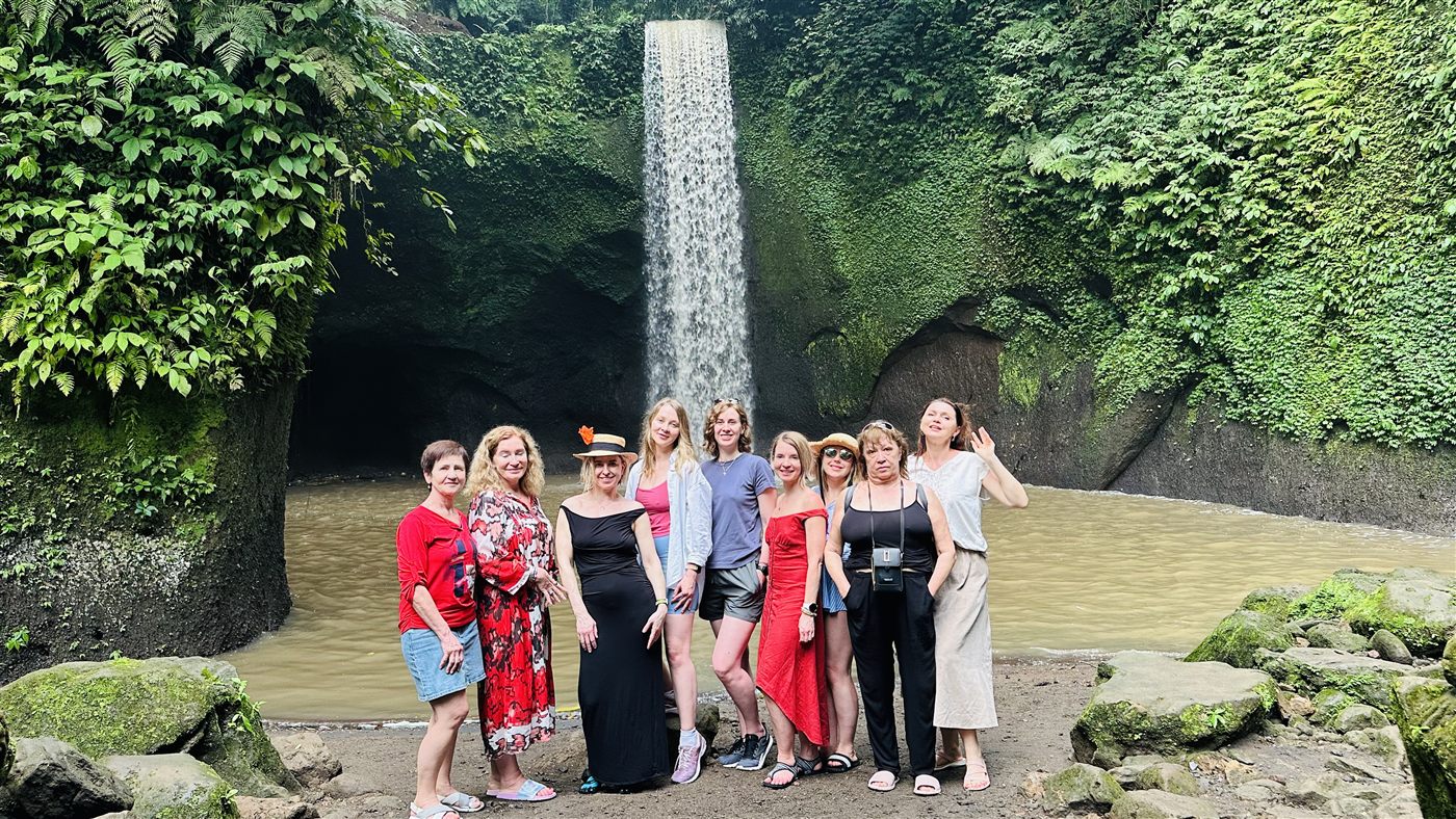 A group standing together at the foot of a tall jungle waterfall