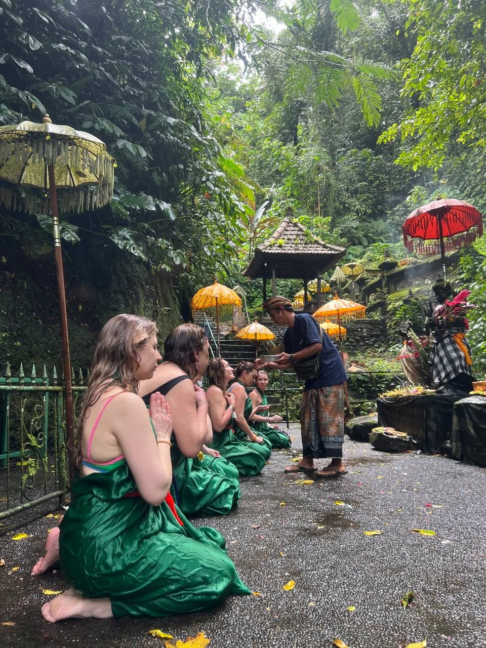 A group kneeling in ceremonial sarongs at a Balinese temple, offerings and umbrellas around them