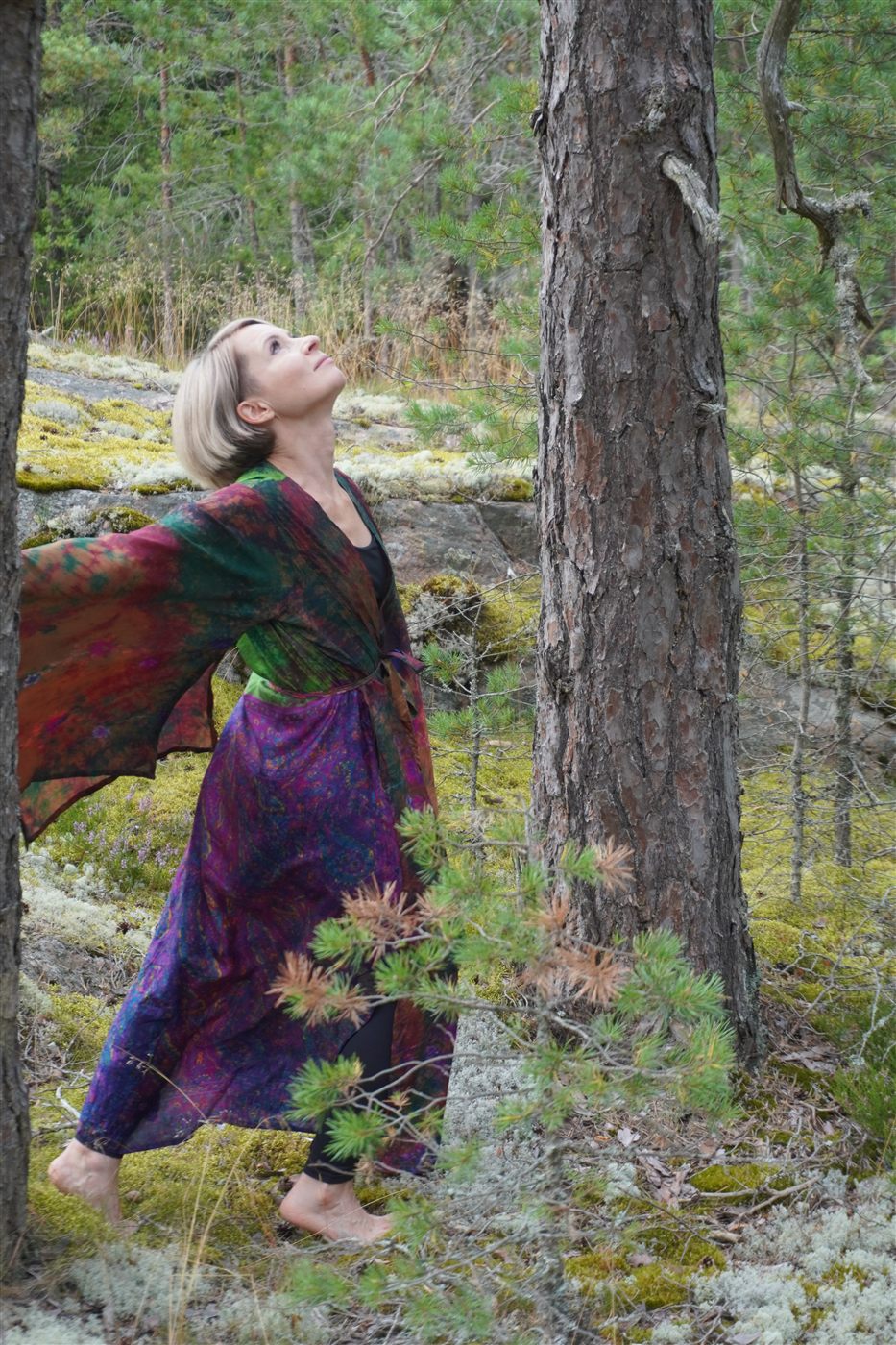 Natasha in a flowing patterned robe, moving between pine trunks in the forest