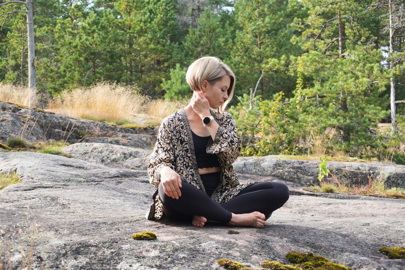 Natasha sitting cross-legged on a moss-covered rock in an open pine forest