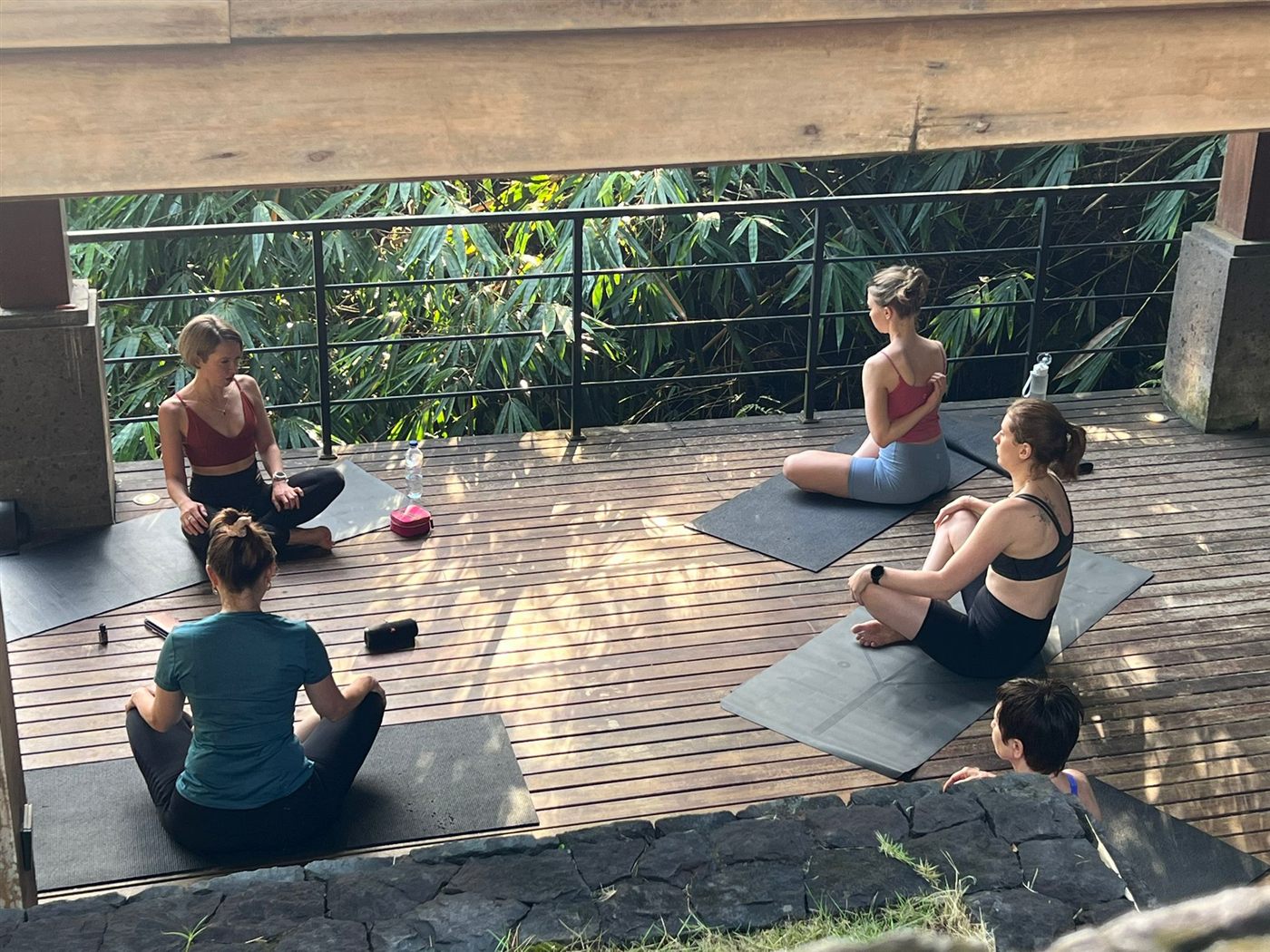 A group sitting on mats on a wide timber deck open to the jungle canopy