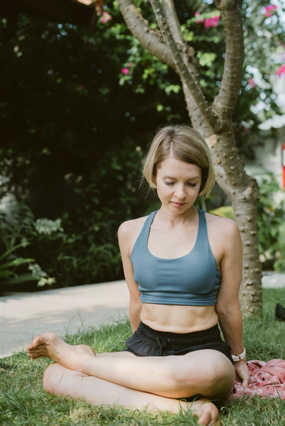 A person sitting cross-legged on the grass in the shade of a tree