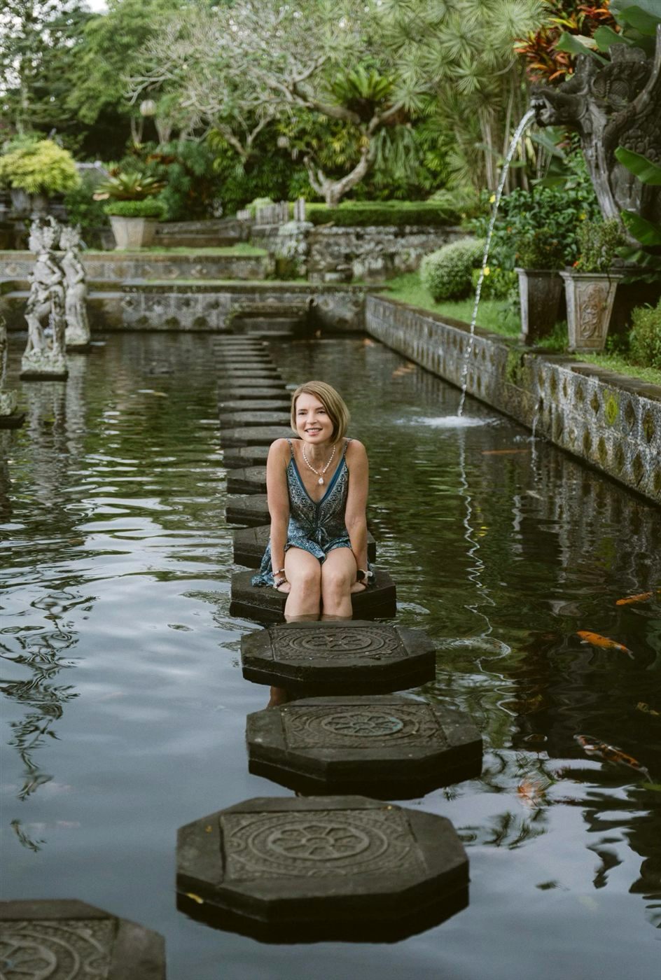 Someone standing on carved stepping stones crossing a lily pond in a Balinese garden