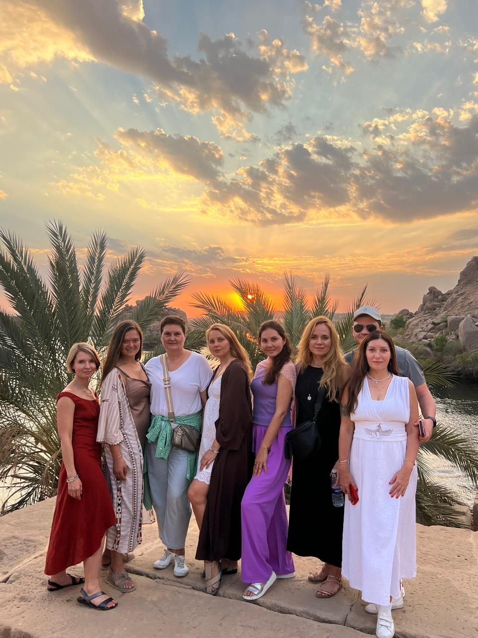 A group standing together against a wide sunset sky, palms behind them