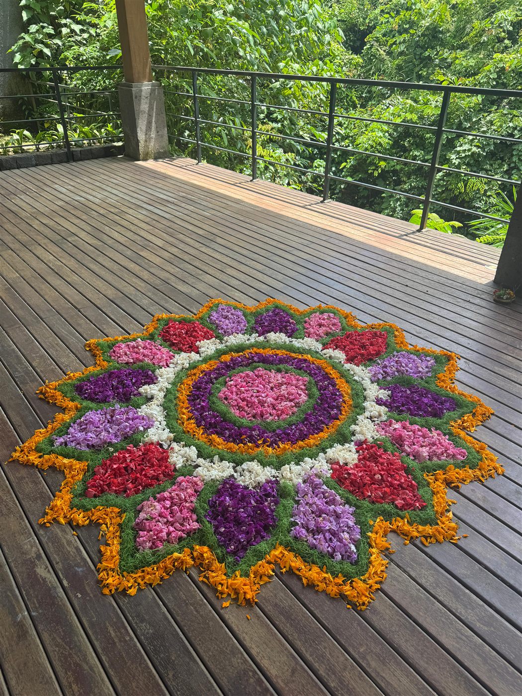A mandala of flowers and leaves laid out on a timber deck above the jungle