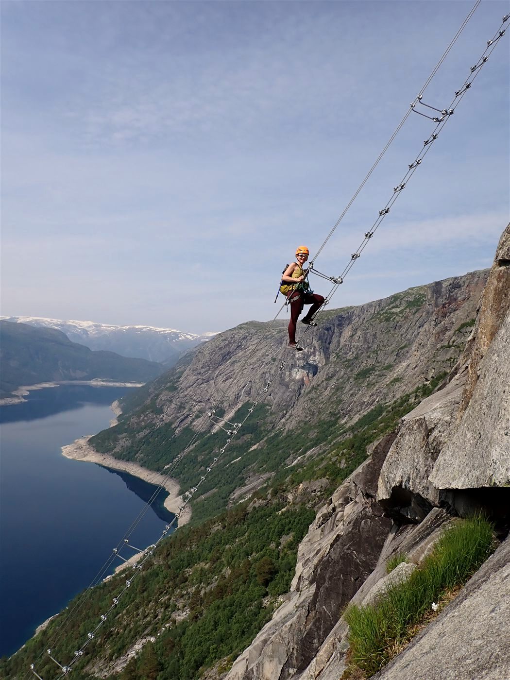 A climber on a via ferrata cable ladder high above a Norwegian fjord