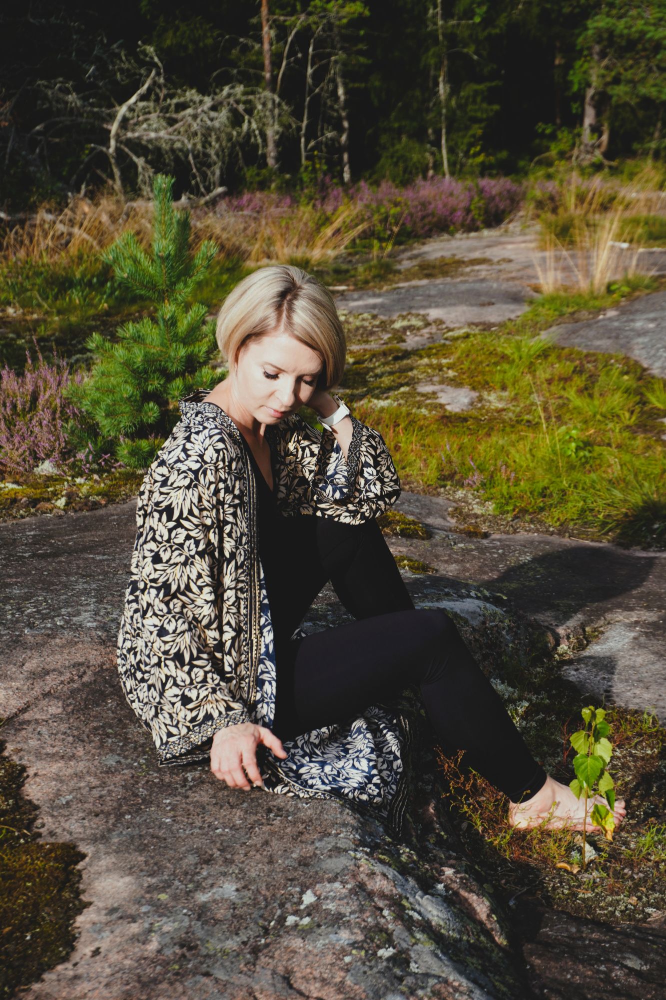 Natasha sitting on a rock outcrop in a Finnish forest, heather in flower behind her