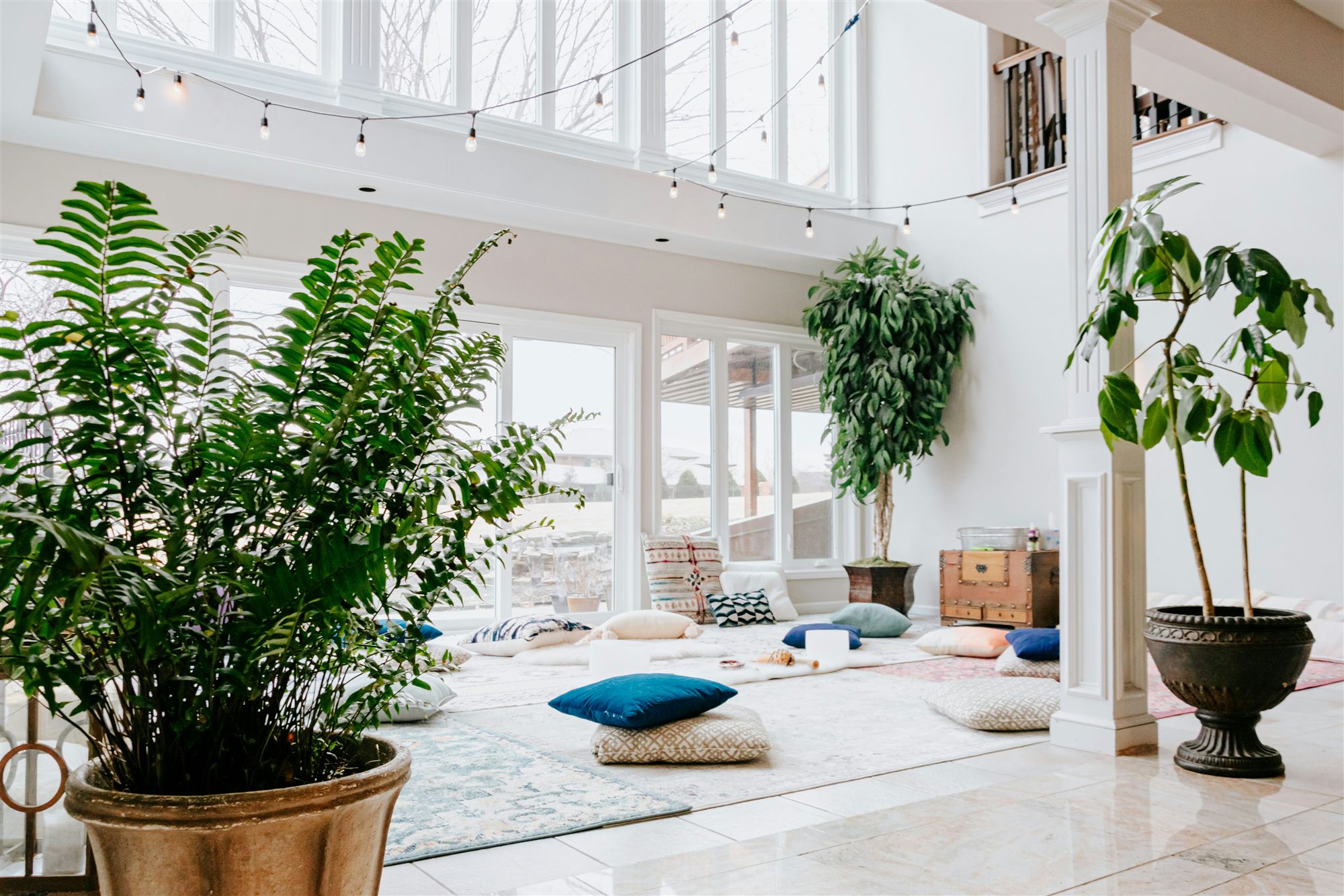 A bright room laid out with floor cushions and plants before a gathering