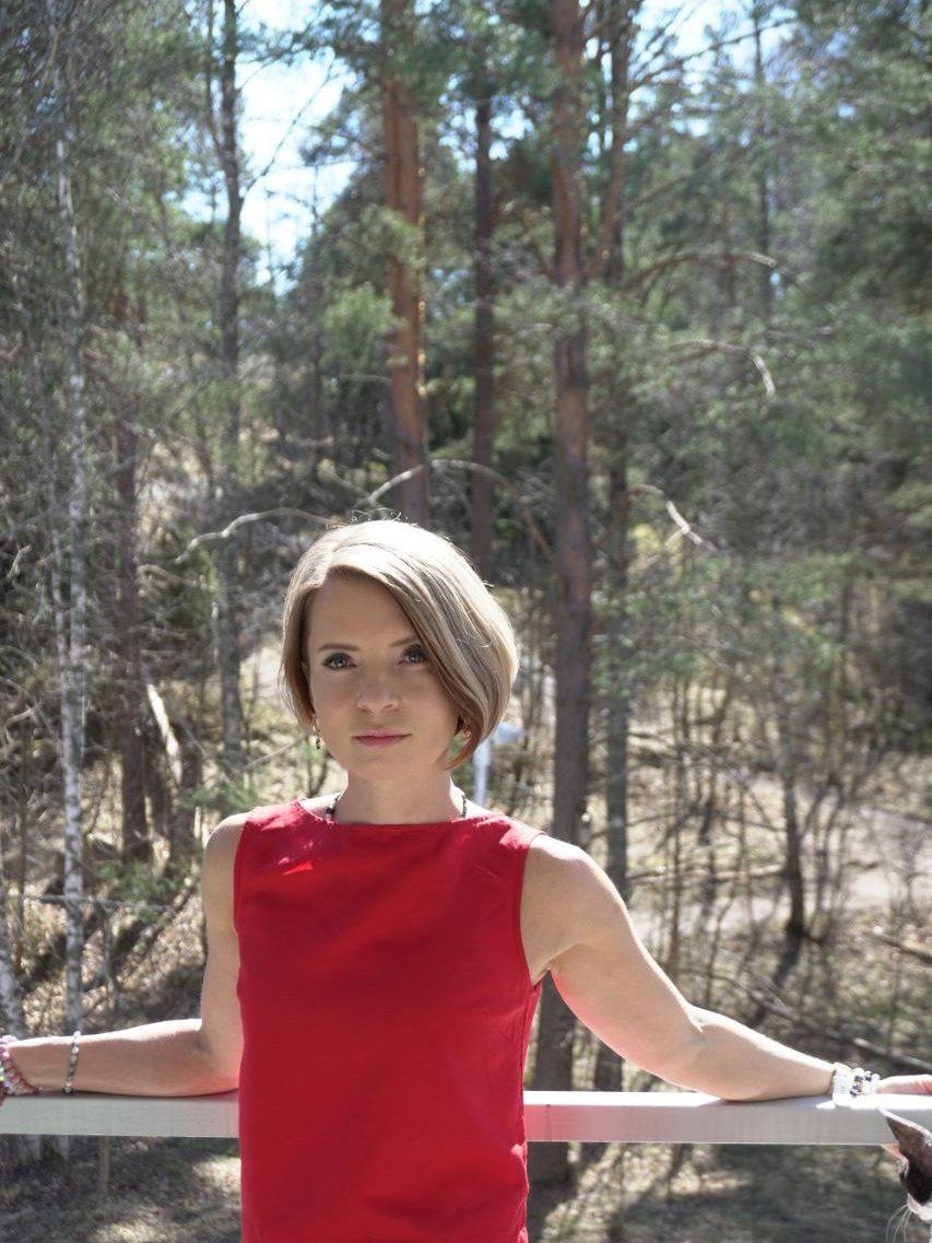 Natasha standing at a railing with pine forest behind