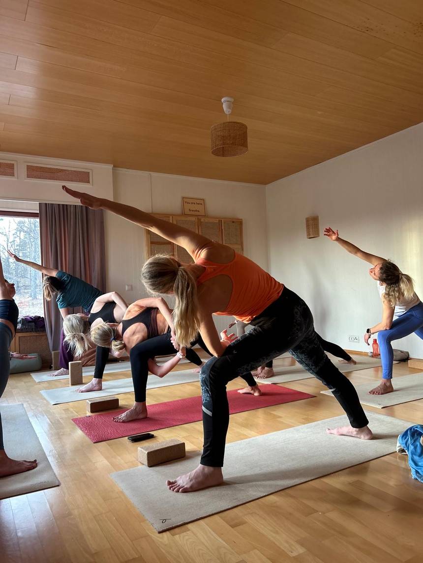 A group practising yoga in a hall with a wooden ceiling